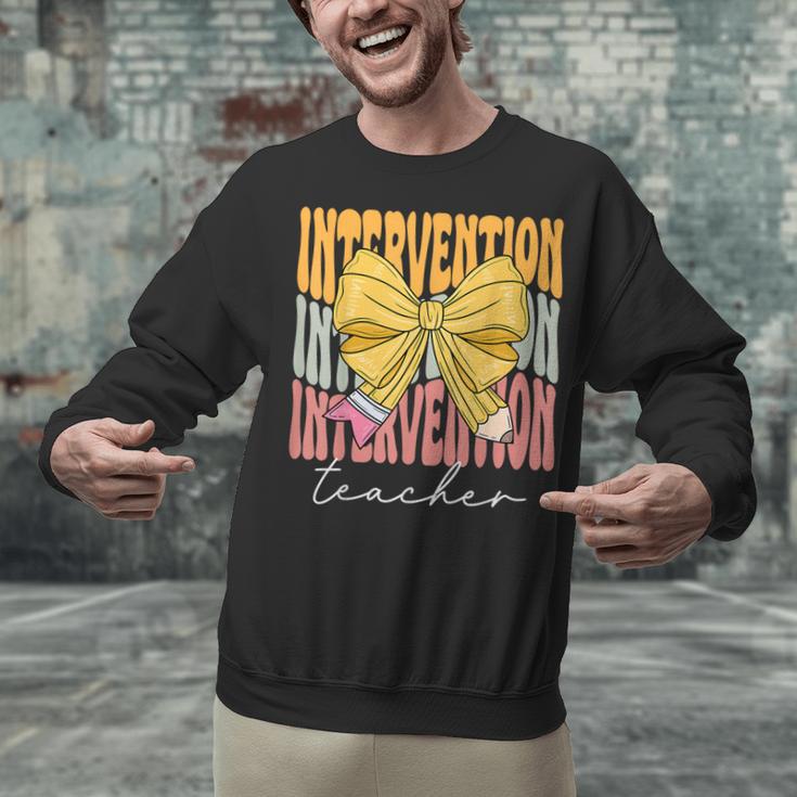 Interventionist Teacher Groovy Coquette Bow Back To School Unisex Sweatshirt, Groovy Teacher Sweatshirts, gift for family, gift for coworker